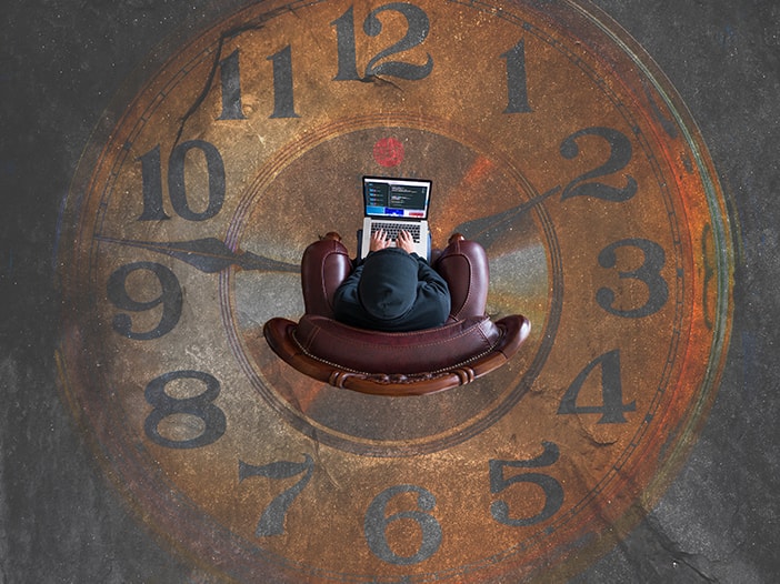 Image of individual coding on a laptop in a chair surrounded by a clockface.